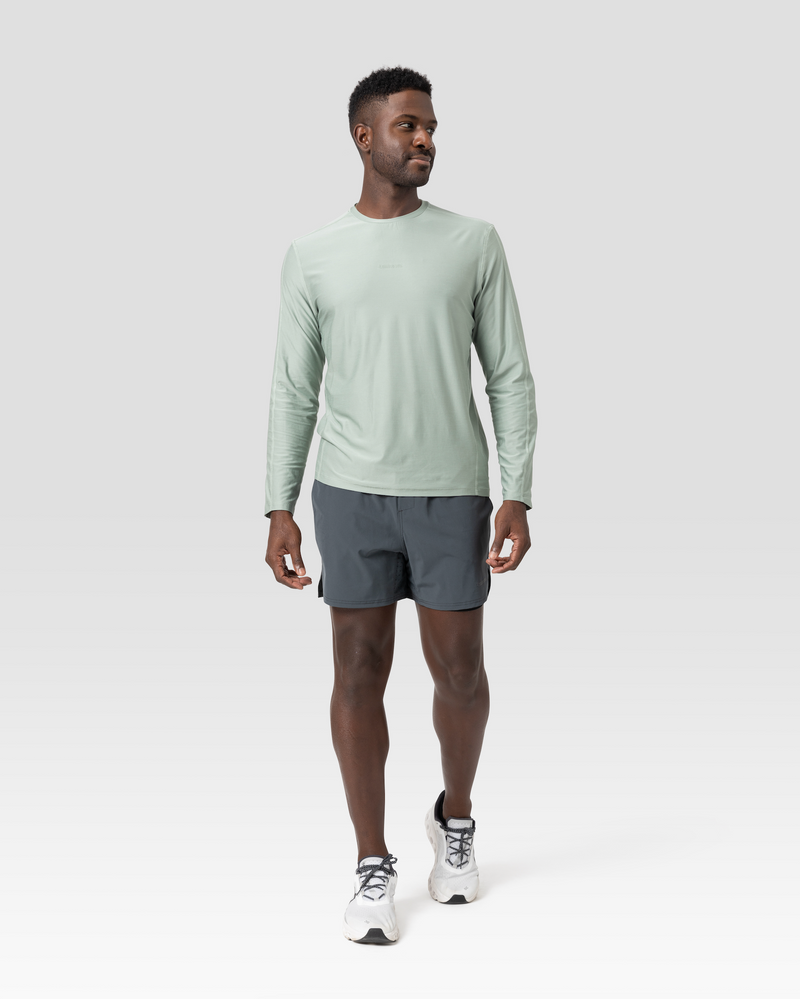 Man wearing a light green long-sleeve shirt and charcoal grey shorts, with sneakers. - Bamboo Ave