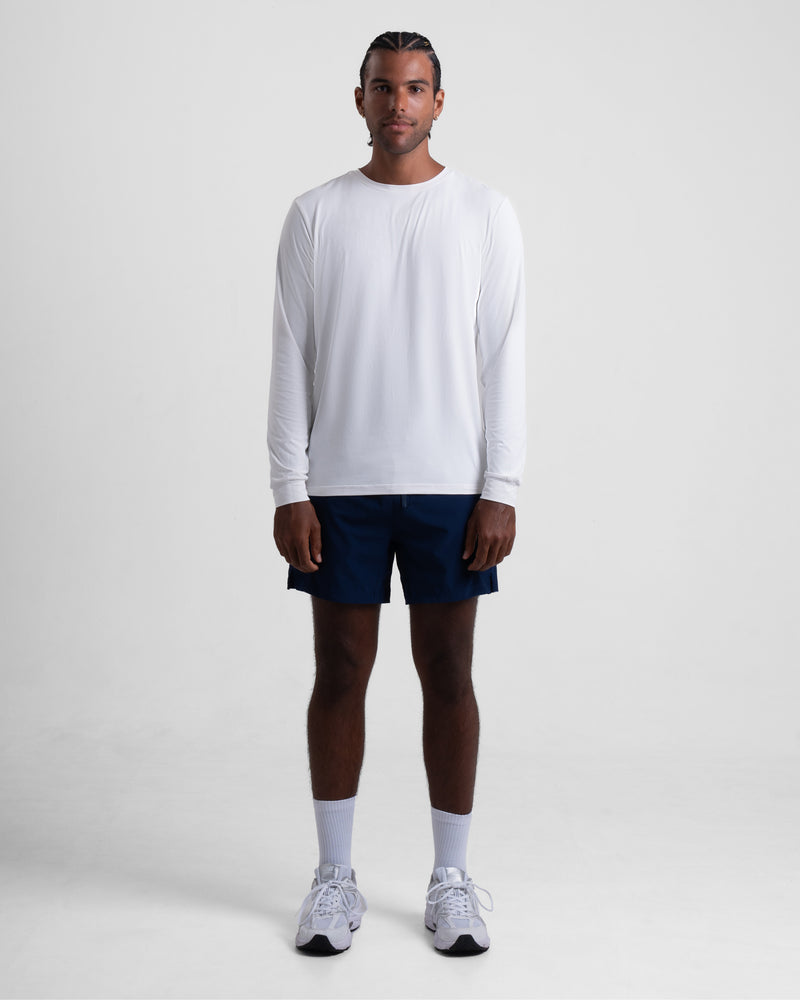Model wearing a long-sleeve white shirt with navy shorts and athletic shoes. - Bamboo Ave